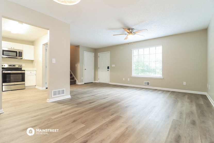 an empty living room with a ceiling fan and a kitchen