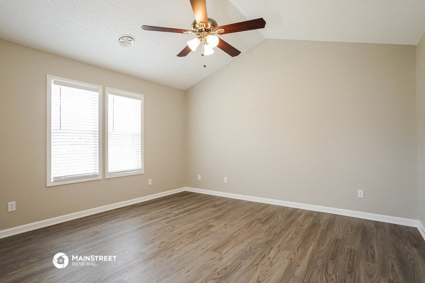 the spacious living room with hardwood flooring and a ceiling fan