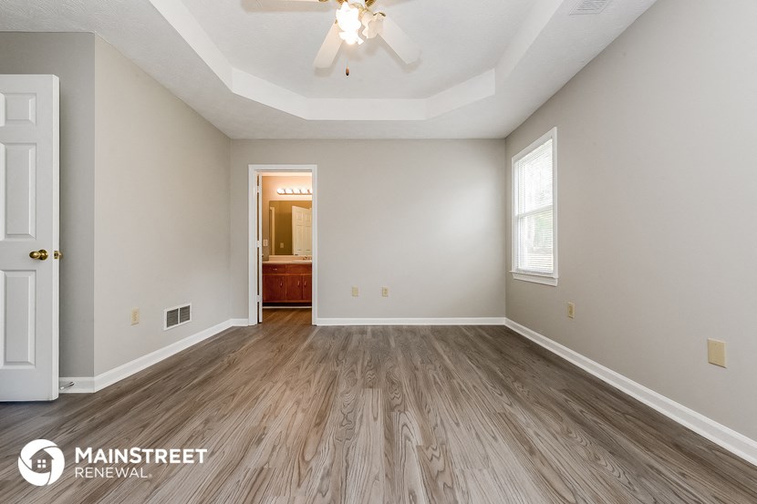 the spacious living room with hardwood flooring and a ceiling fan