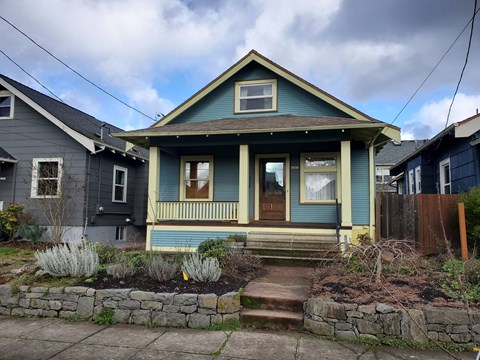 A blue house with a front porch and a stone wall.