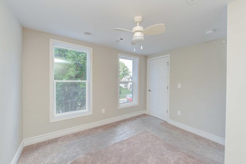 an empty living room with a ceiling fan and two windows