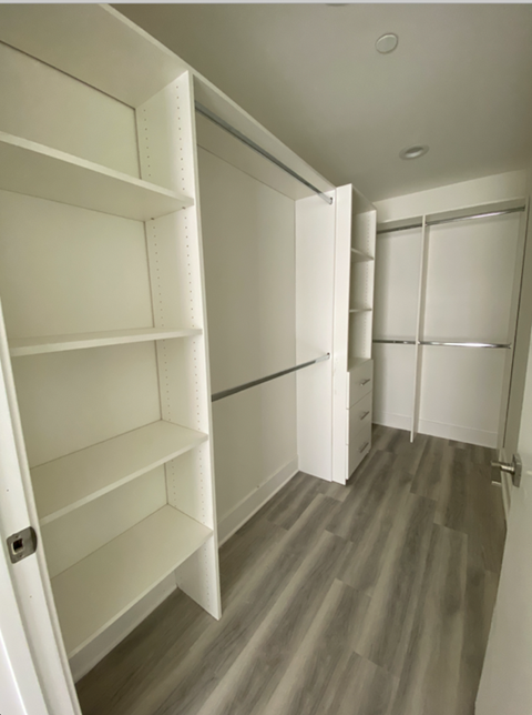 a walk in closet with white shelves and a wood floor