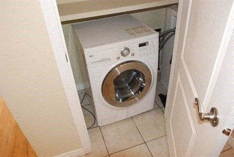 A white washing machine is in a small space under a door.