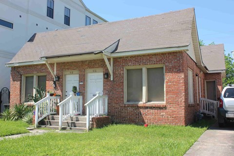 A small red brick house with a white door and a white porch.