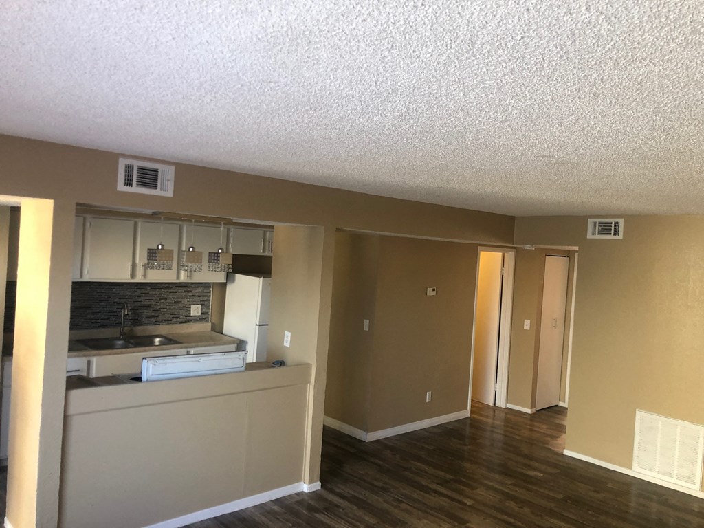 an empty living room with a kitchen and a hard wood floor