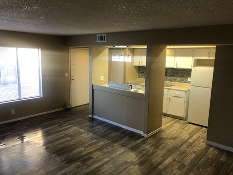 an empty living room with a kitchen and a window