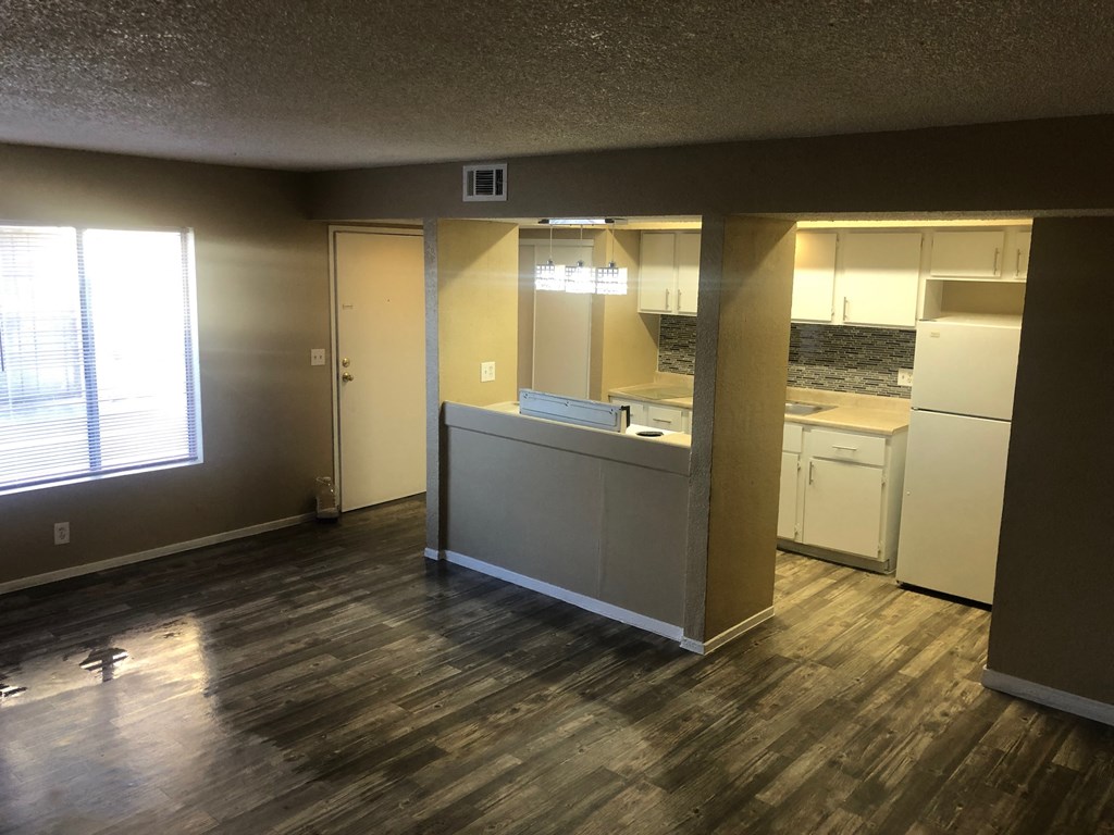 an empty living room with a kitchen and a window