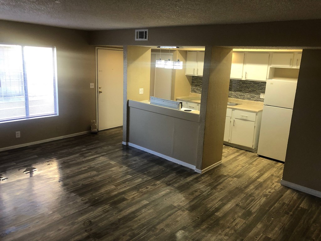 an empty living room with a kitchen and a window