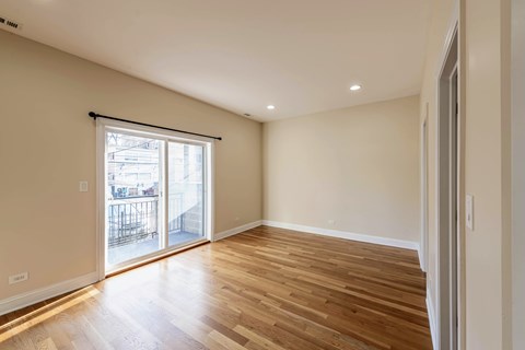 A room with wooden floors and a sliding glass door leading to a balcony.