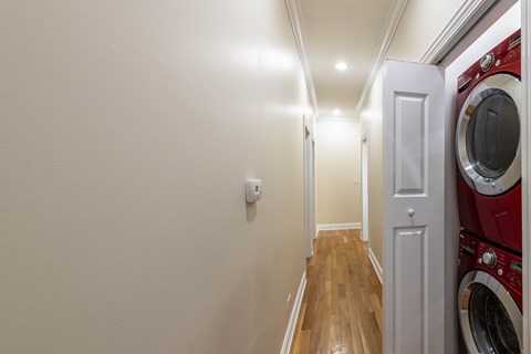 A red washing machine is on the right side of a white door in a narrow hallway.