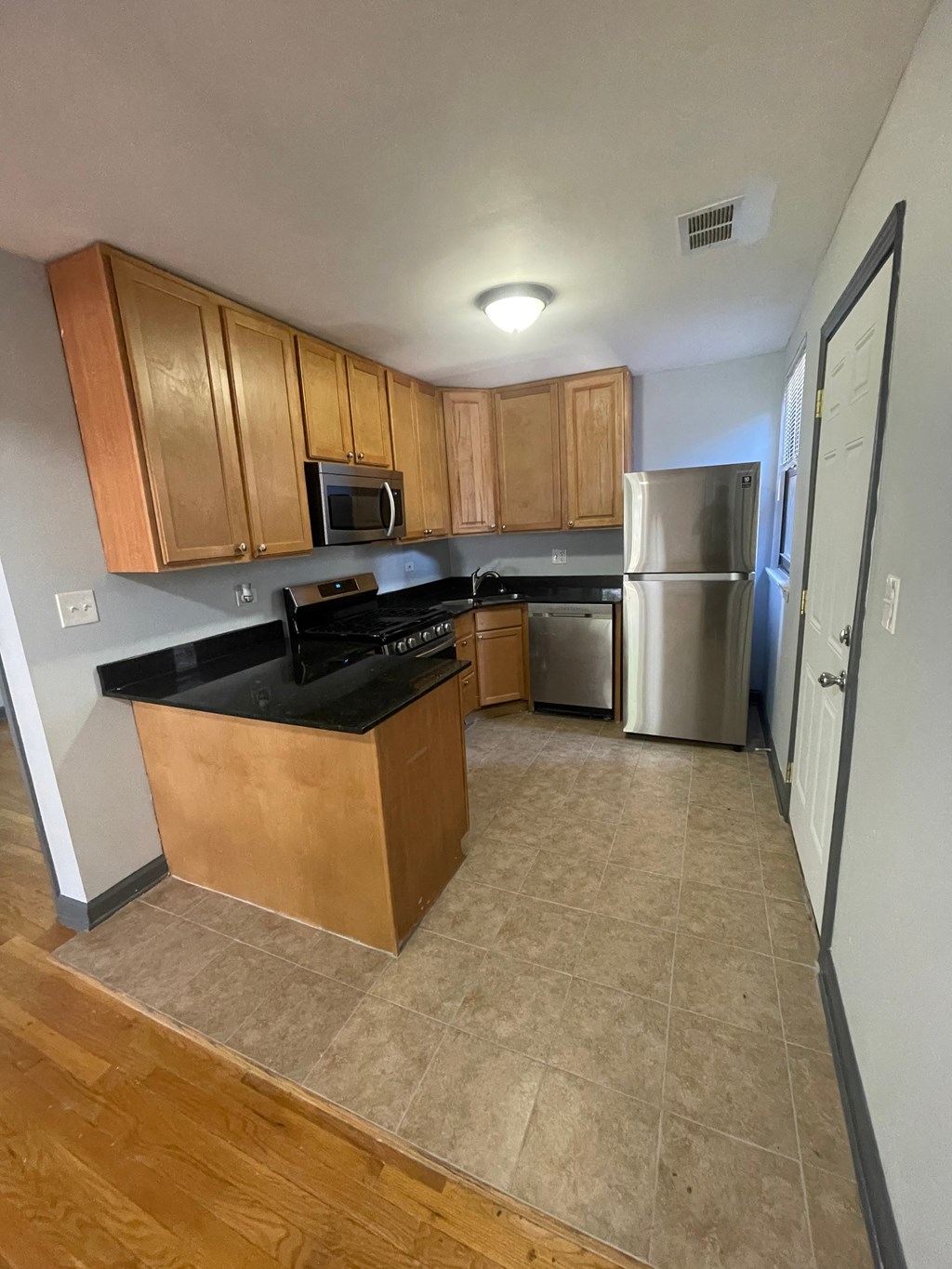 an empty kitchen with wooden cabinets and a stainless steel refrigerator