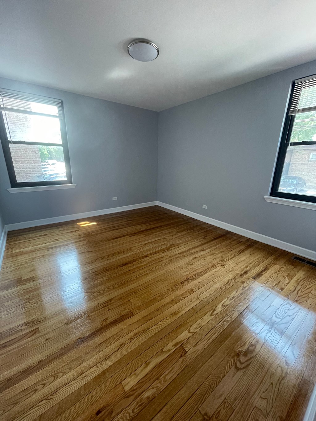 an empty room with wooden floors and two windows