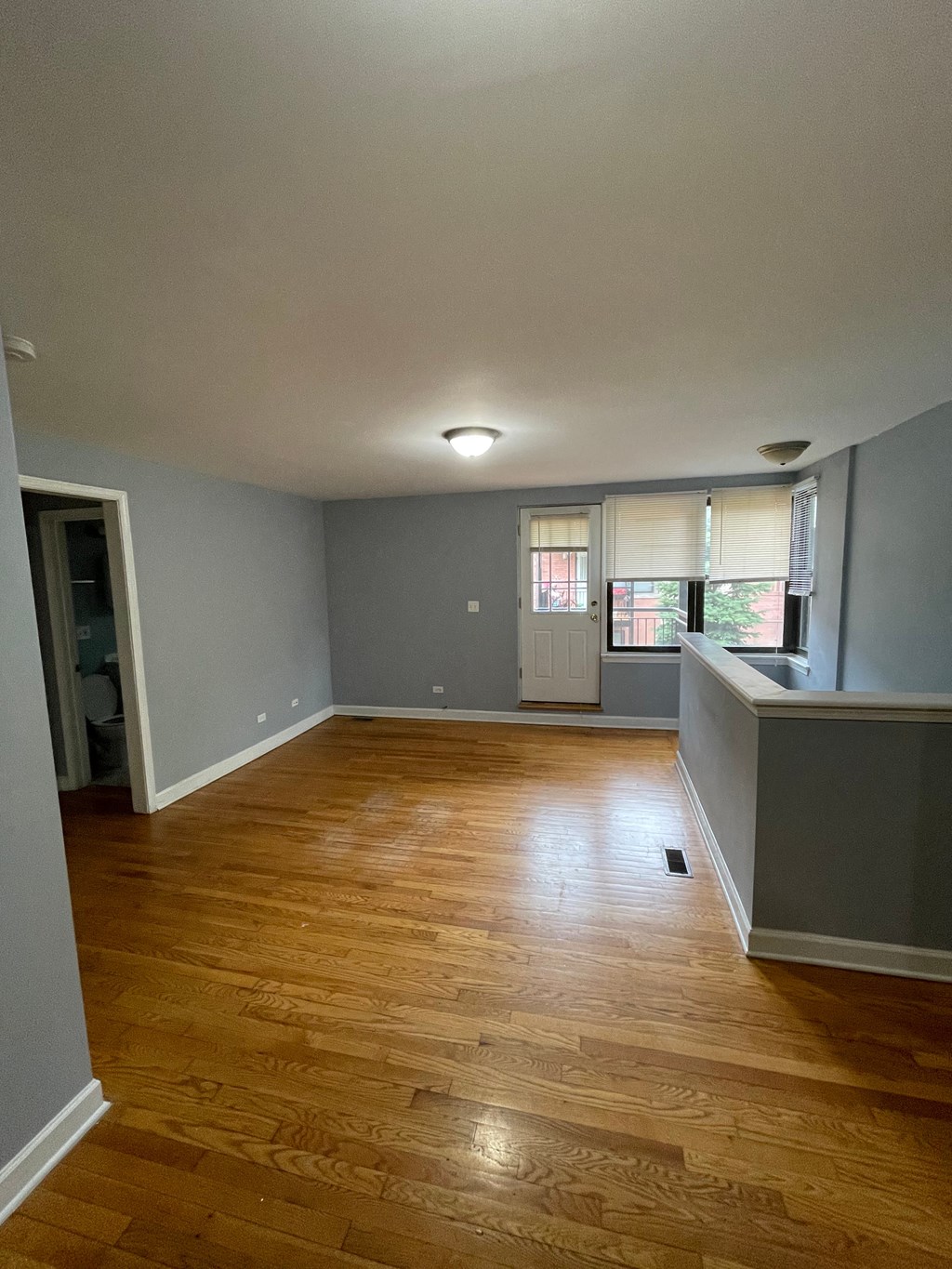 an empty living room with wood floors and a kitchen