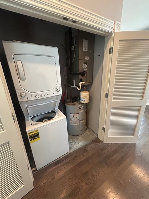 A white washing machine is in a small space between a wall and a door.