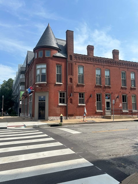 A red brick building with a turret sits on a corner.