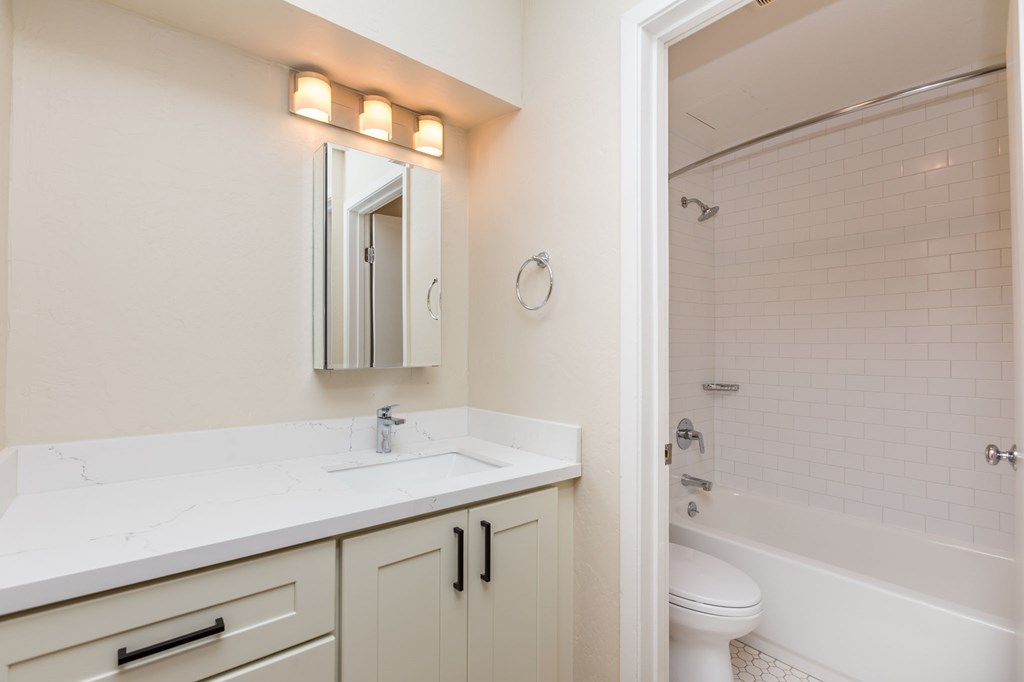 A white bathroom with a sink, mirror, toilet and bathtub.