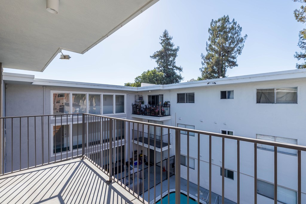A balcony with a metal railing and a pool in the background.