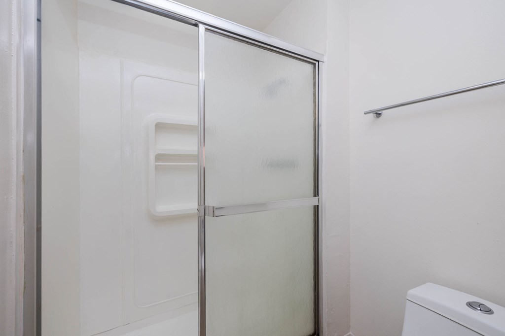 A white toilet is in a small bathroom with a glass shower door.