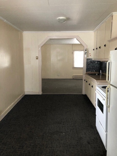 an empty kitchen with white appliances and black carpet
