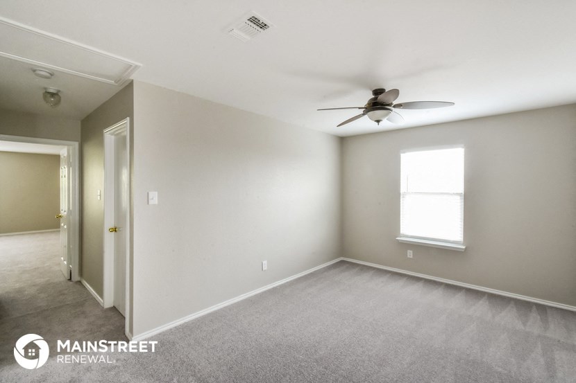 the living room of an apartment with carpet and a ceiling fan