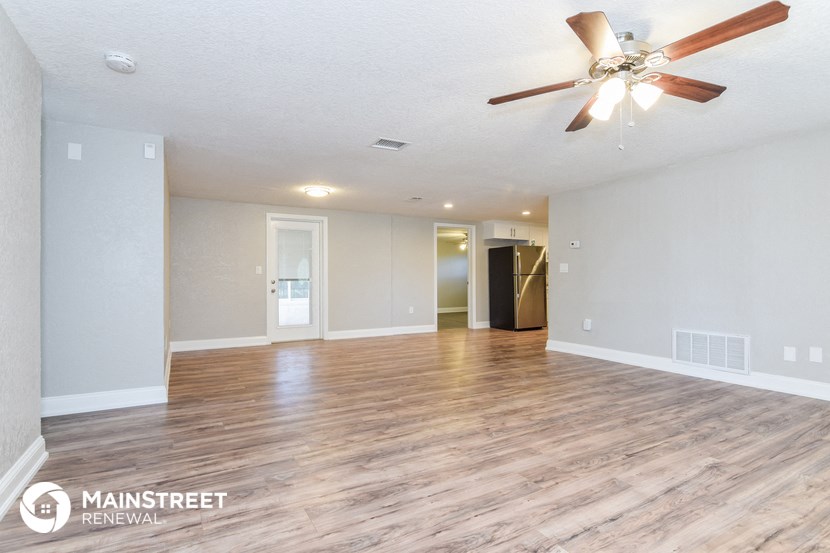 the spacious living room with hardwood flooring and a ceiling fan