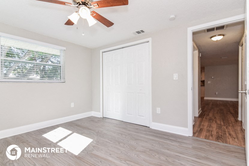 an empty living room with a ceiling fan and a door to a hallway