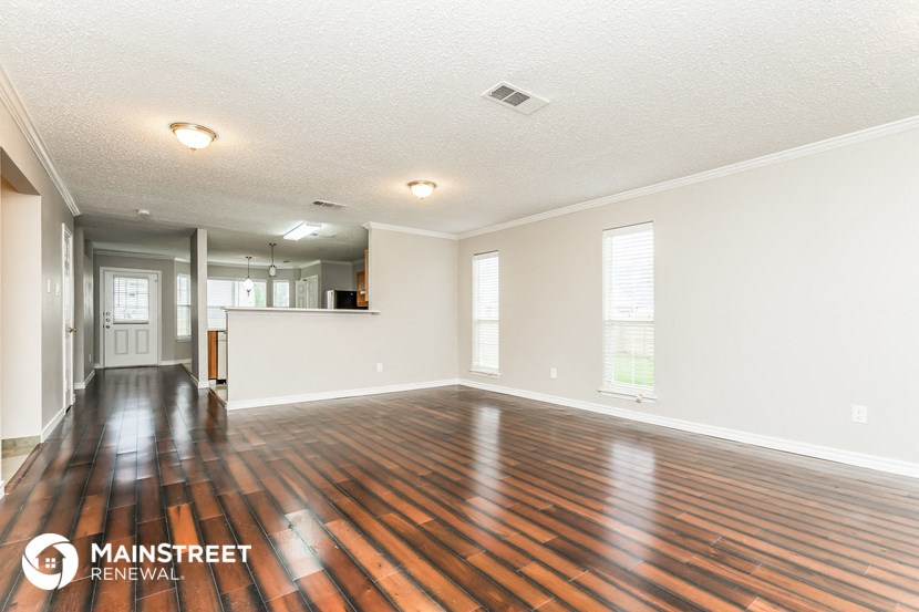 an empty living room with wood flooring and a kitchen