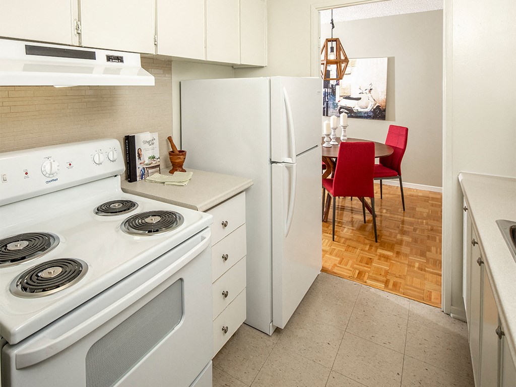 a kitchen with a white stove and refrigerator and a dining room with a red chair