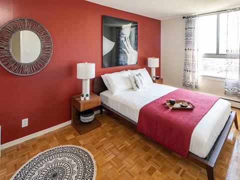 a bedroom with a red wall and a bed with a white comforter