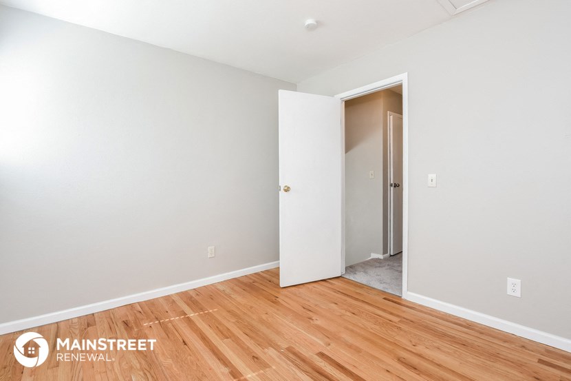 a bedroom with white walls and wood flooring and an open door