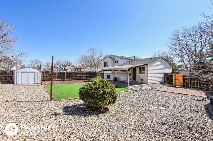 a backyard with a white house and a yard with a green lawn