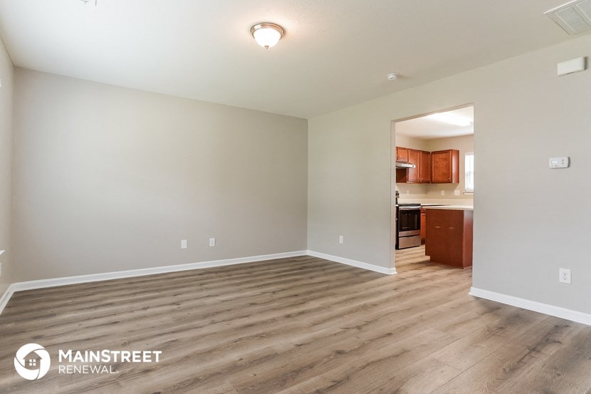a spacious living room with wood flooring and a kitchen