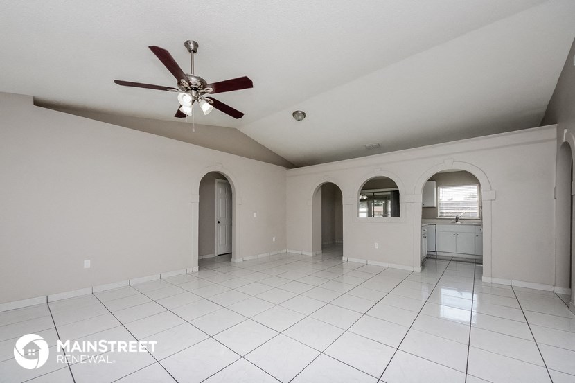 an empty living room with white tiles and a ceiling fan