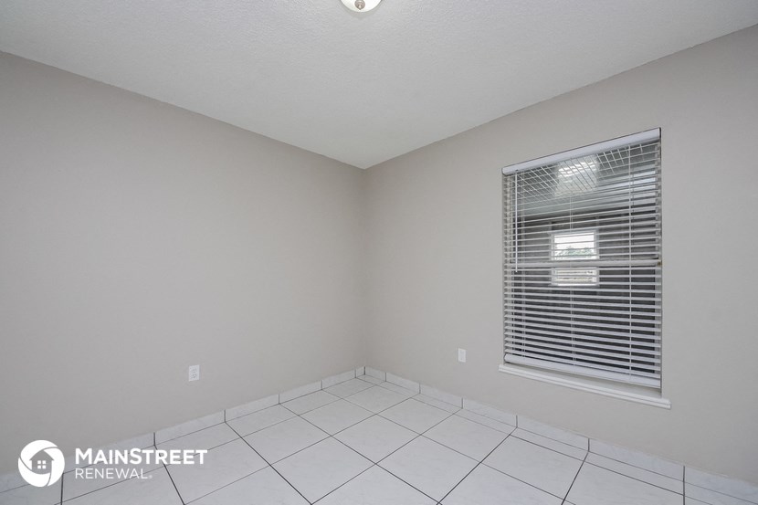 the spacious living room with white tile flooring and a window