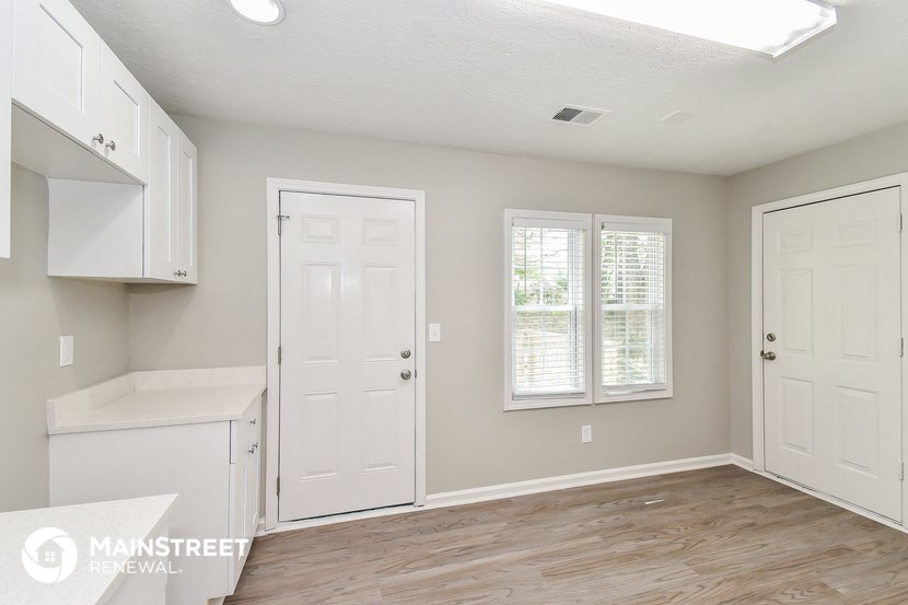 an empty kitchen with white cabinets and a white door and window