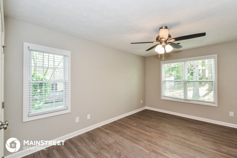 an empty living room with a ceiling fan and two windows
