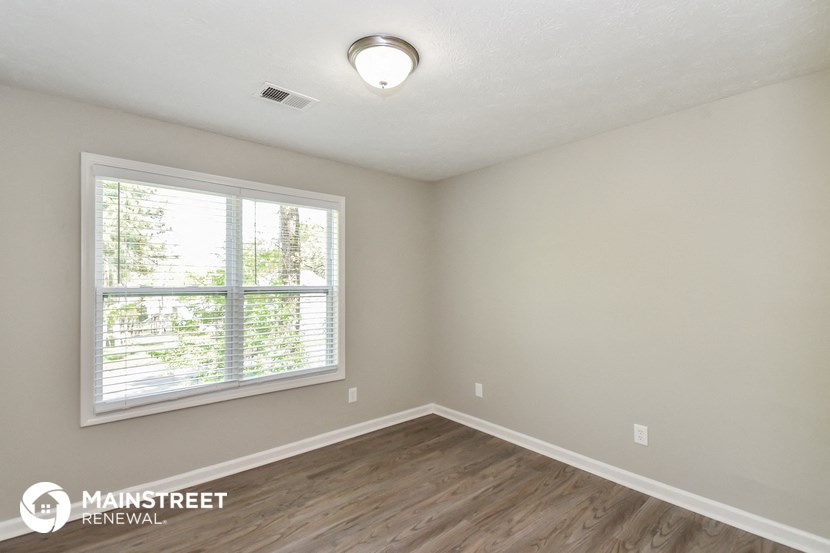 an empty bedroom with a large window and wood flooring