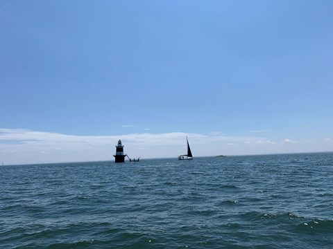 A lighthouse stands in the distance on a calm sea with a sailboat nearby.