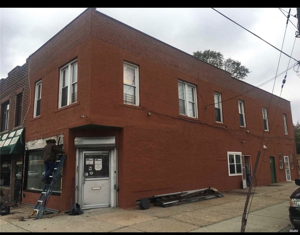 A man is on a ladder painting the front of a red brick building.