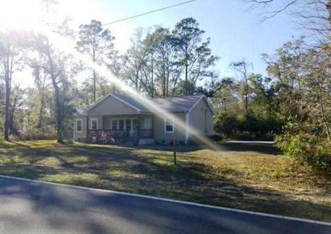 A house with a white roof and a porch is surrounded by trees.