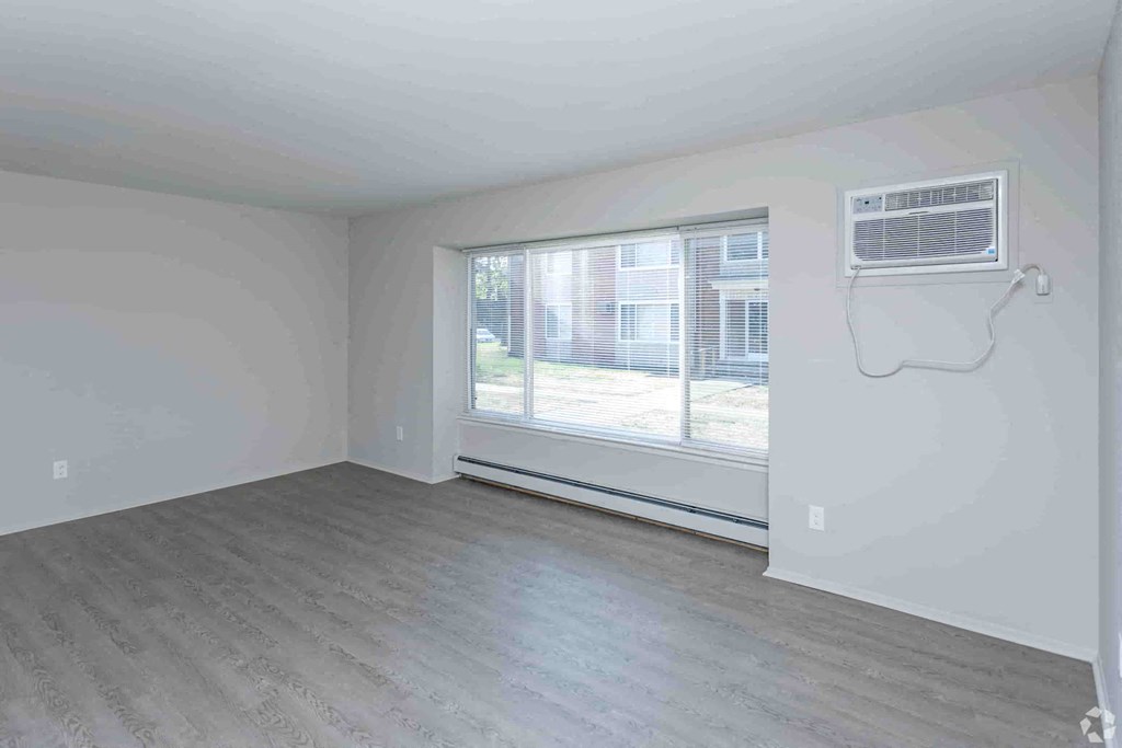 an empty living room with a window and a air conditioner