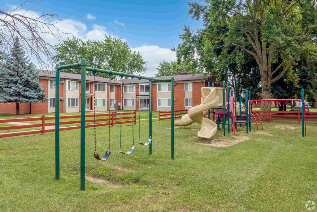 a playground with a slide and swings in front of an apartment building