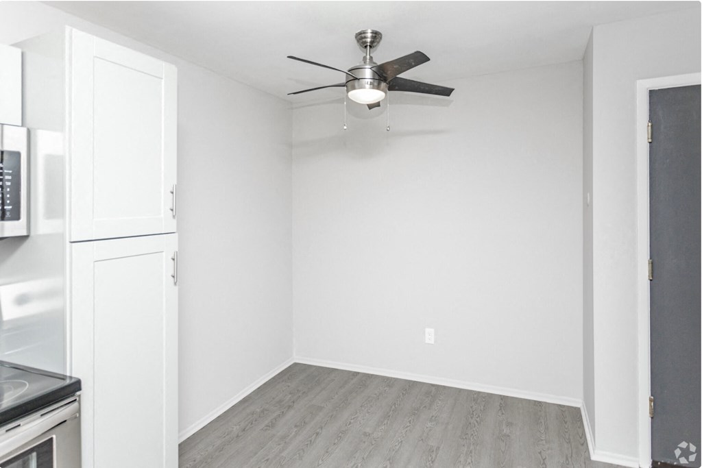 an empty room with a ceiling fan and a kitchen