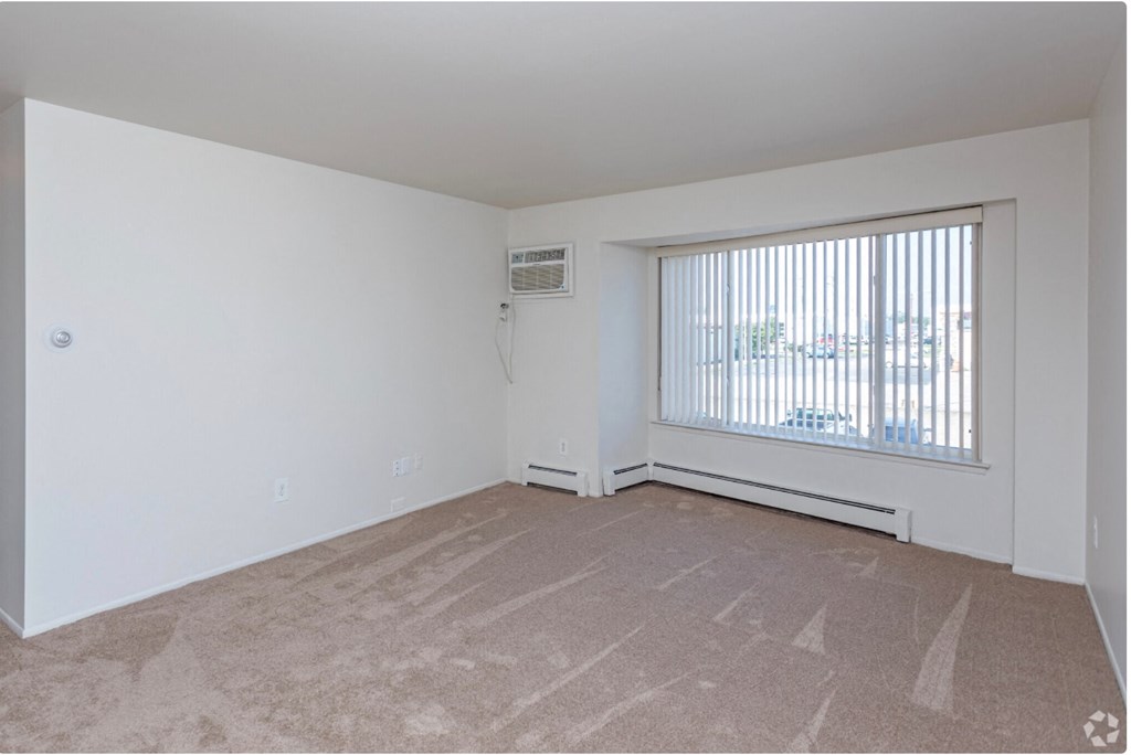 the living room of an apartment with a large window and carpeting