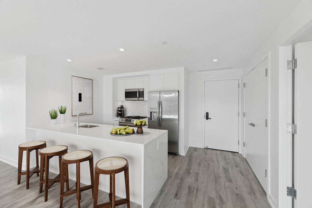 a white kitchen with a white counter top and three wooden stools