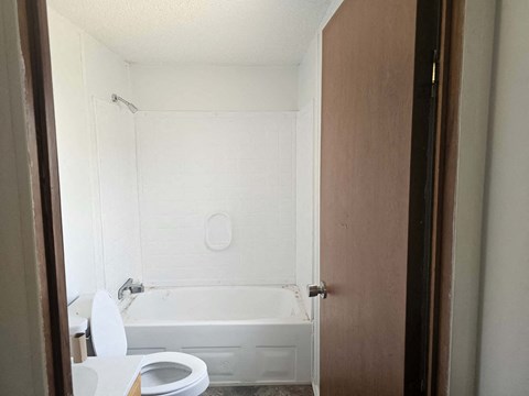 A white toilet is in a small bathroom with a white tub.