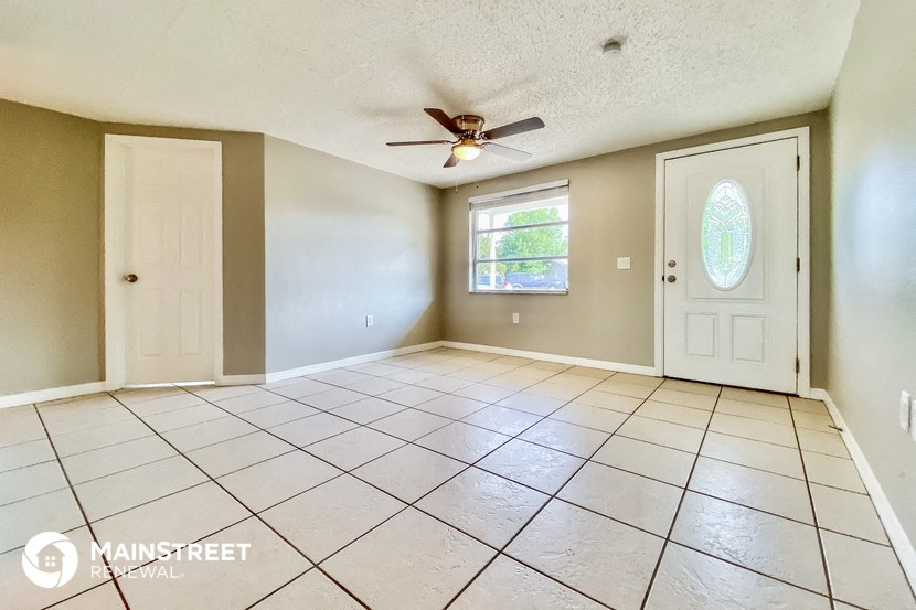 an empty living room with a ceiling fan and tiled floors