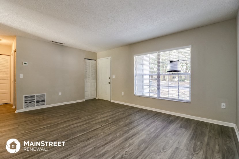 the living room of an apartment with wood flooring and a large window