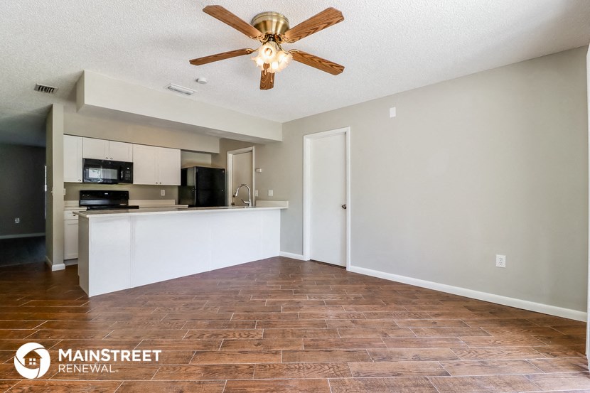 the living room and kitchen of a rental house with a ceiling fan