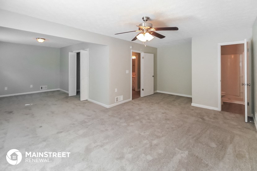 an empty living room with a ceiling fan and a hallway